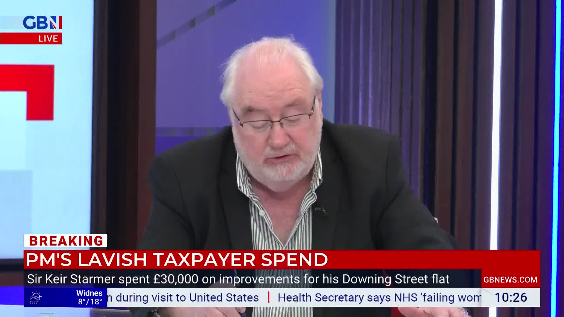 A man with white hair and glasses speaks into a microphone, his gaze directed downwards. Behind him, a screen displays "GBN LIVE" and a breaking news headline about taxpayer spending.