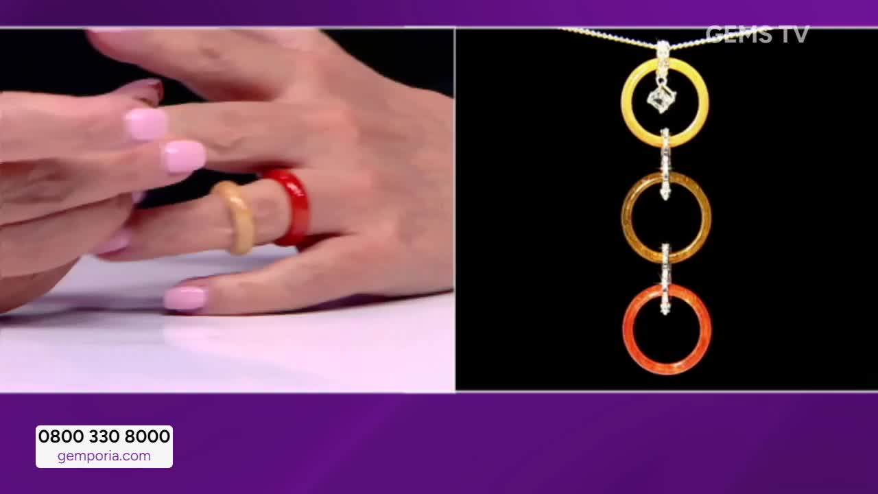 A hand on Gems TV displays two rings, one red and one yellow, on a finger. To the right, a necklace with three matching colored rings hangs against a black background.

