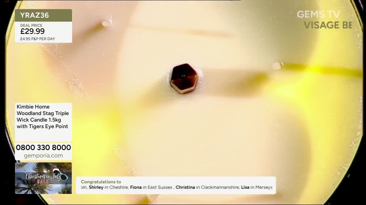 A close-up of a candle is on display, with a dark, hexagonal stone embedded in the wax. The Gems TV logo is visible, along with details about the product and a list of viewer congratulations.
