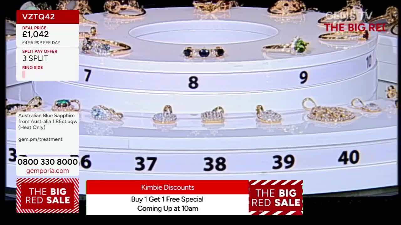 On the Gems TV set, a rotating display of jewelry is visible, with rings and swan-shaped pendants catching the light. The screen flashes details about a sapphire ring deal, alongside information about a "Big Red Sale" and a "Buy 1 Get 1 Free Special" coming soon.
