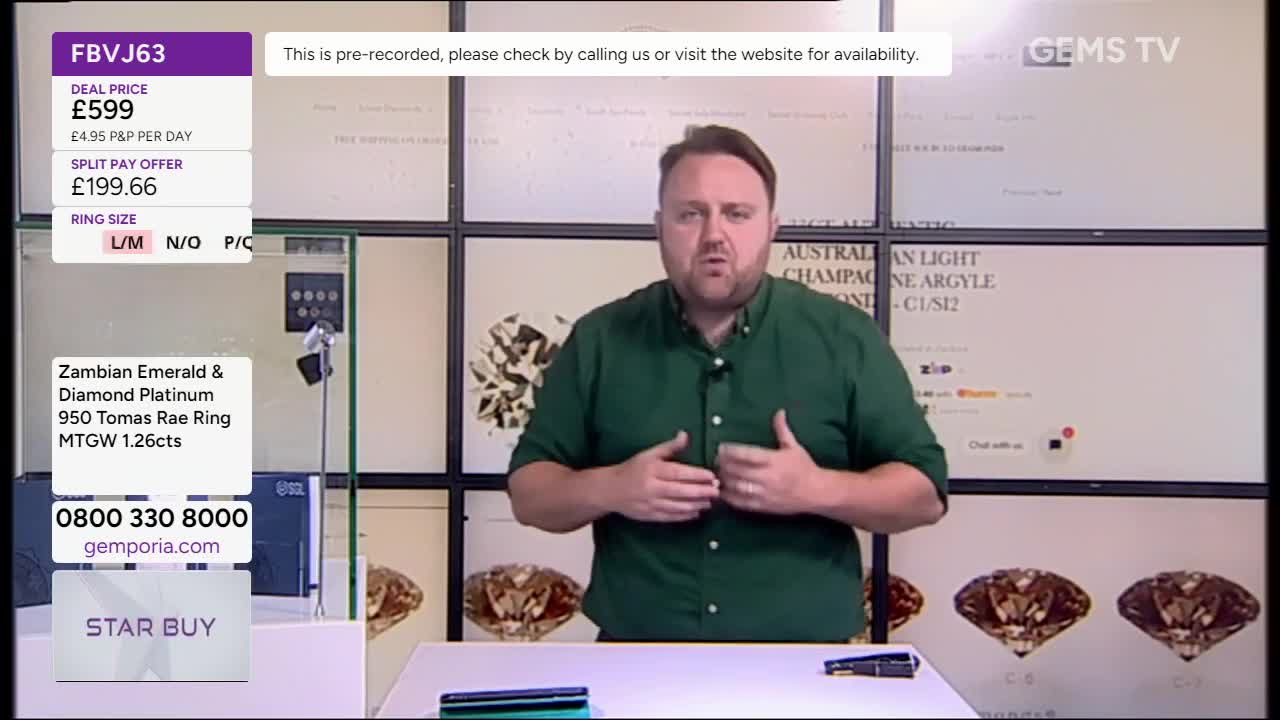 A man in a green shirt gestures with his hands, talking directly to the camera. Behind him, a screen displays a deal for a ring on Gems TV.
