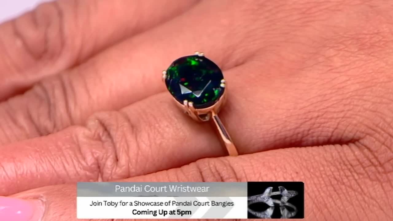 A hand holds a gold ring, the large, dark gemstone catching the light. A Gems TV graphic at the bottom advertises a bangle showcase coming up at 5pm.
