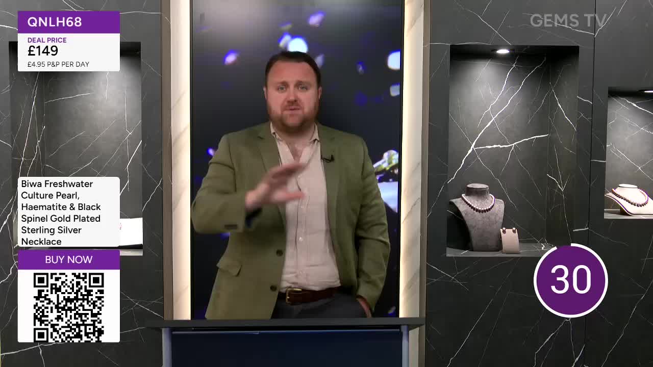 A man in a green jacket gestures with his right hand, speaking to the camera. Behind him, jewelry is displayed in illuminated niches, and a countdown timer ticks down.
