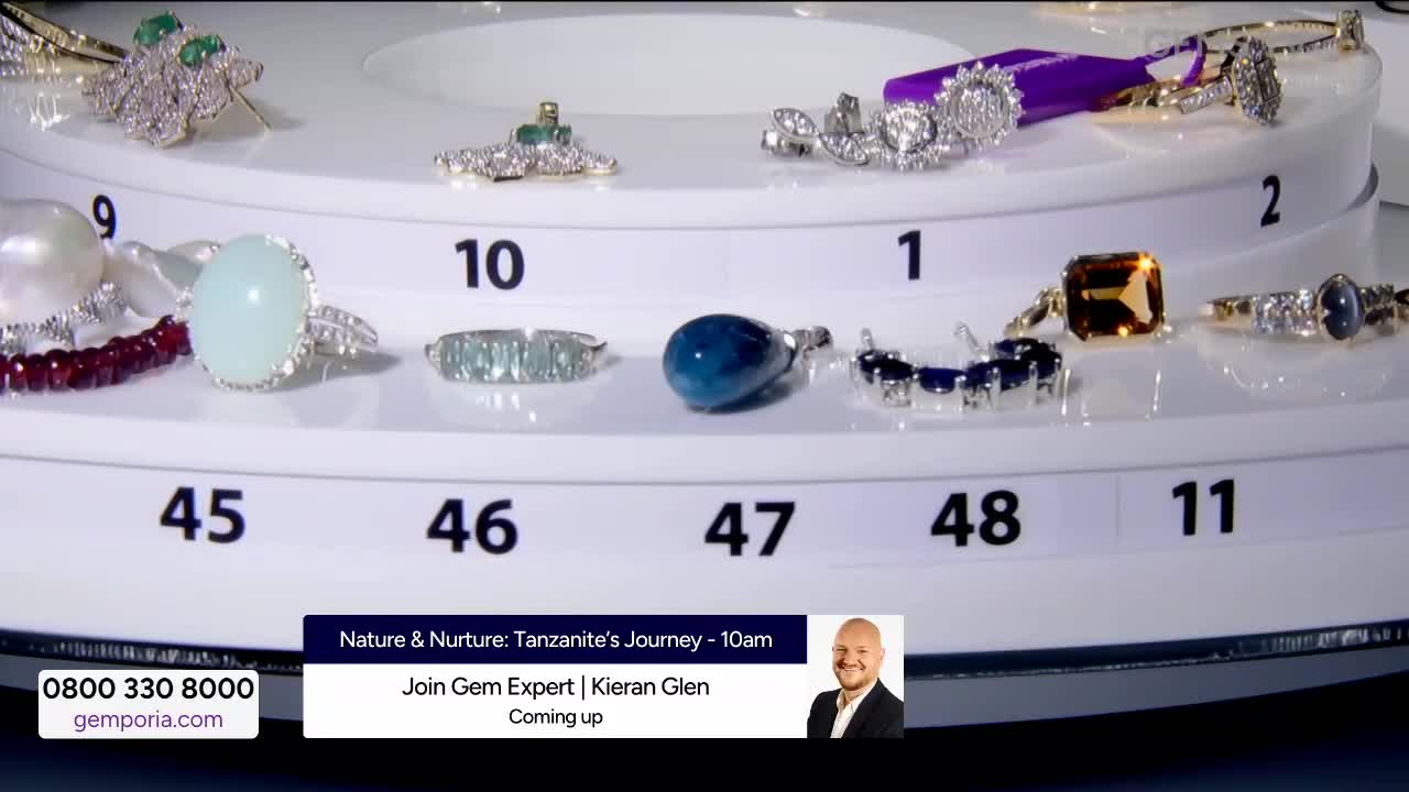 A rotating display of jewelry, each piece numbered, is set against a bright background. A banner at the bottom advertises a "Tanzanite's Journey" segment on Gems TV.
