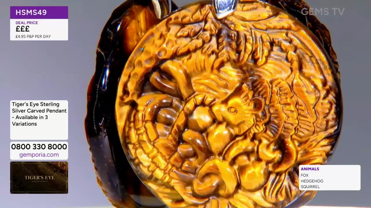 A large, carved tiger's eye pendant dominates the screen, its intricate design catching the light. The Gems TV logo is visible, along with a price tag and a list of animals.
