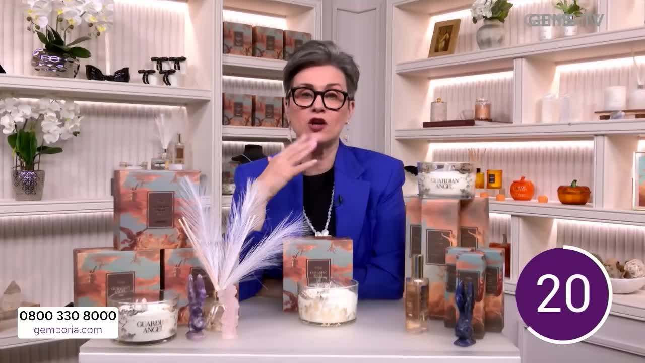 A woman in a blue blazer gestures with her hand as she presents a selection of candles and fragrances. The Gems TV logo is visible in the corner, along with a countdown timer.
