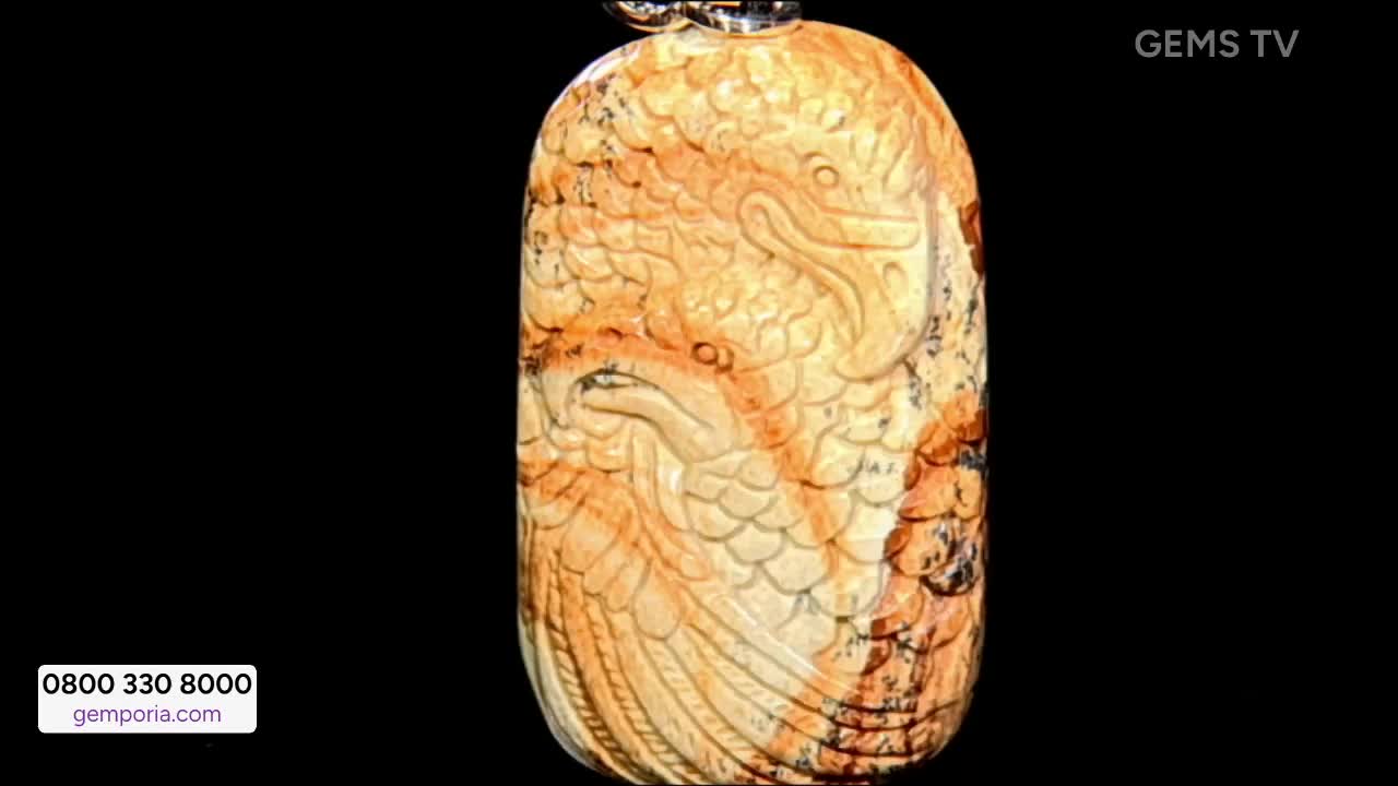 On Gems TV, a pendant carved with a bird design is displayed against a black background. The stone is a light brown color with darker veins, and the intricate carving is highlighted.
On Gems TV, a pendant carved with a bird design is displayed against a black background. The stone is a light brown color with darker veins, and the intricate carving is highlighted.
