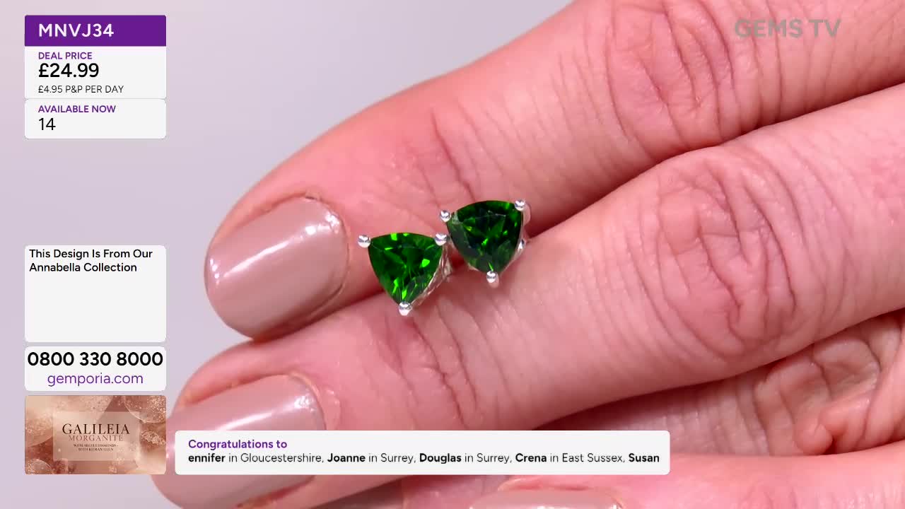 A pair of emerald-green, triangular earrings are held up for the camera on Gems TV. The presenter's fingers, with neatly manicured nails, cradle the jewelry.
A pair of emerald-green, triangular earrings are held up for the camera on Gems TV. The presenter's fingers, with neatly manicured nails, cradle the jewelry.