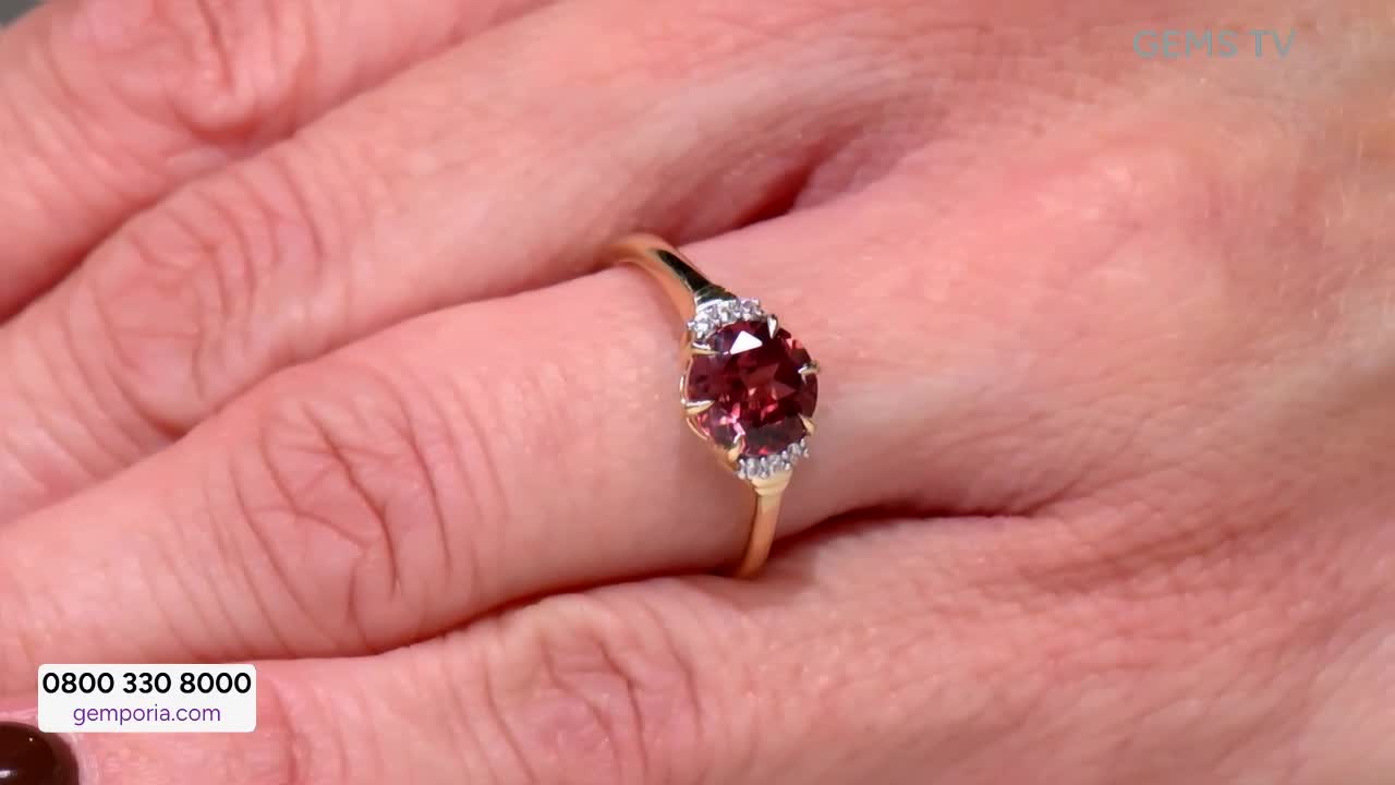 On Gems TV, a hand displays a gold ring with a large, oval, red gemstone flanked by smaller white stones. The ring is held up, catching the light as if ready to be sold.
On Gems TV, a hand displays a gold ring with a large, oval, red gemstone flanked by smaller white stones. The ring is held up, catching the light as if ready to be sold.