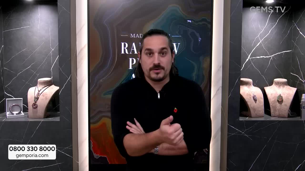 The man in the black sweater gestures with his hands as he speaks on Gems TV. Behind him, jewelry is displayed on mannequins in illuminated alcoves.
The man in the black sweater gestures with his hands as he speaks on Gems TV. Behind him, jewelry is displayed on mannequins in illuminated alcoves.