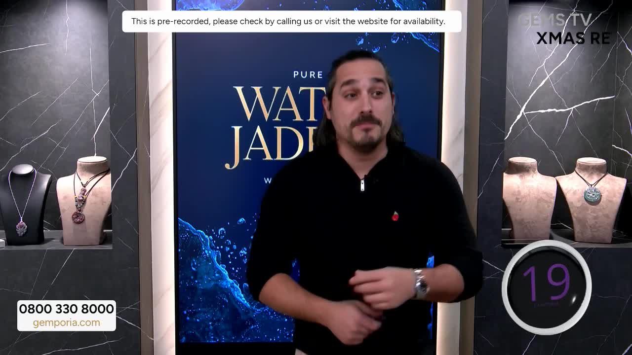 A man in a black sweater stands in front of a backdrop advertising "Water Jade" from Gems TV. A countdown timer ticks down as he speaks, and necklaces are displayed on stands to his left and right.
