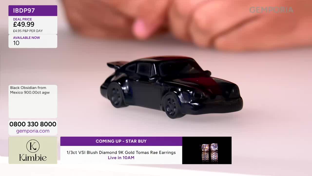 A polished black obsidian car, a miniature Porsche, sits on a bright surface. Fingers hover just above it, ready to pick it up.