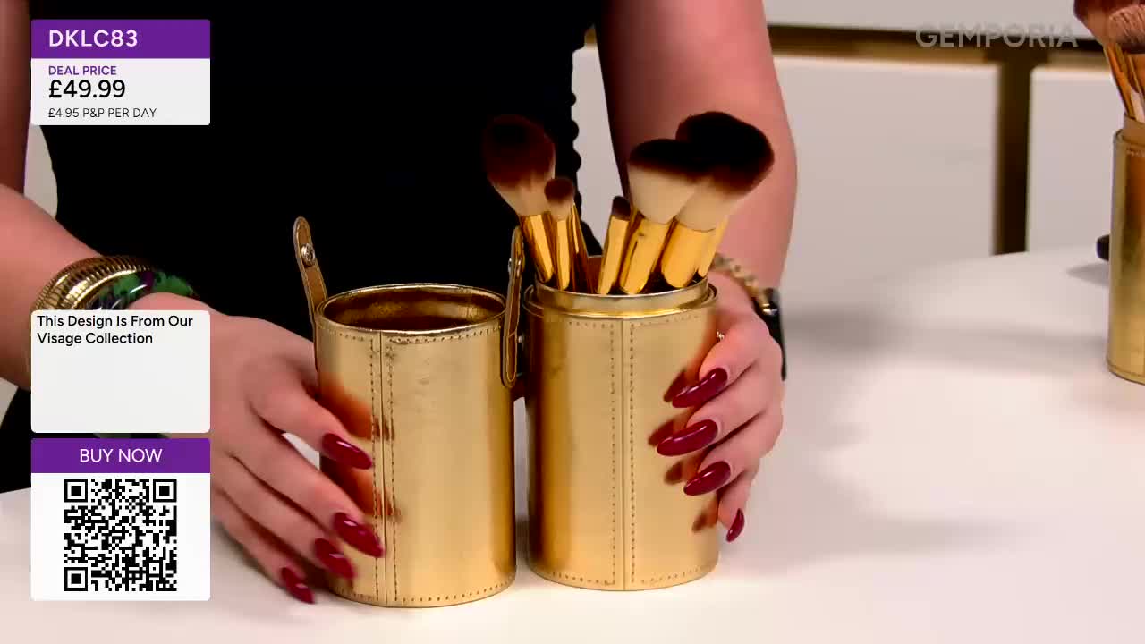 A hand with long, red nails holds a gold cylindrical case filled with makeup brushes. Another identical case sits empty beside it.