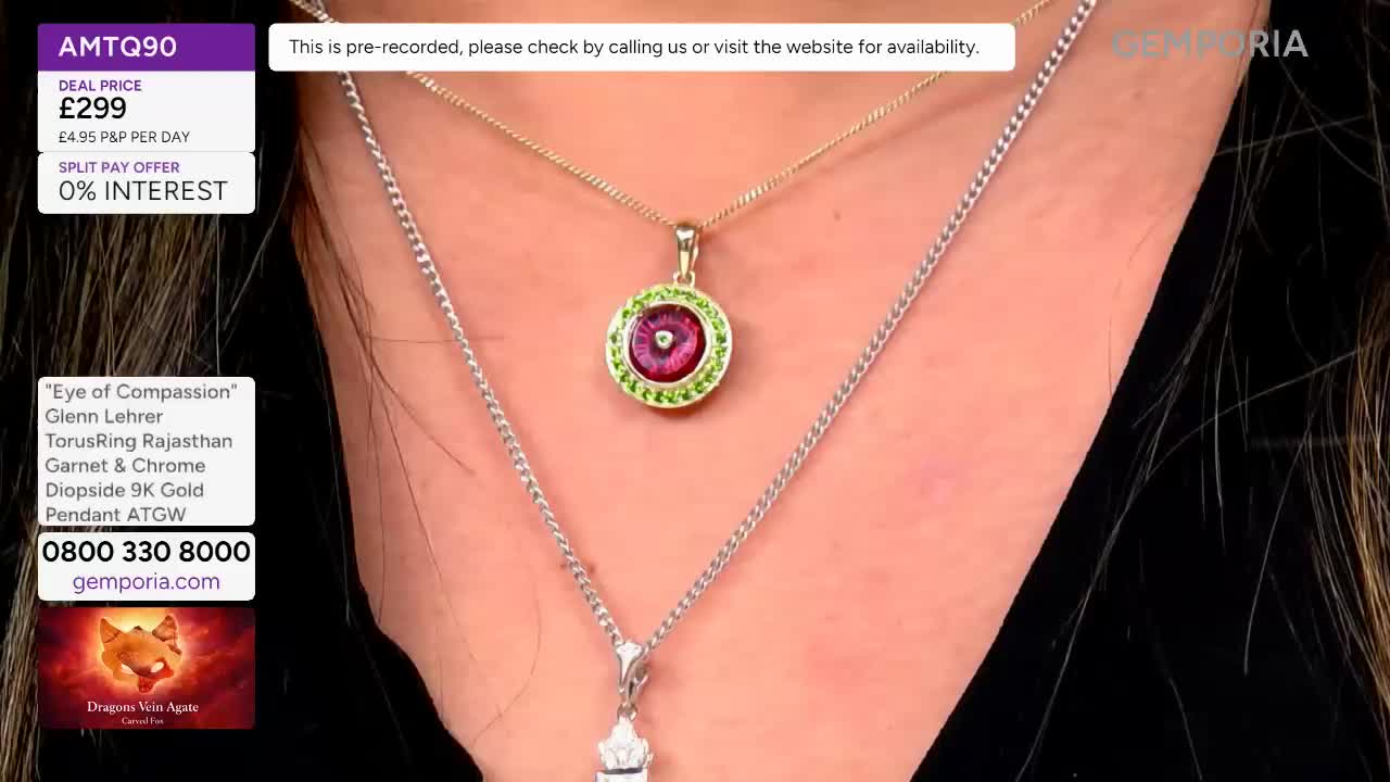 A gold chain with a circular pendant, featuring a deep pink stone surrounded by green gems, rests on a silver chain. The pendant hangs just below the collarbone, catching the light.