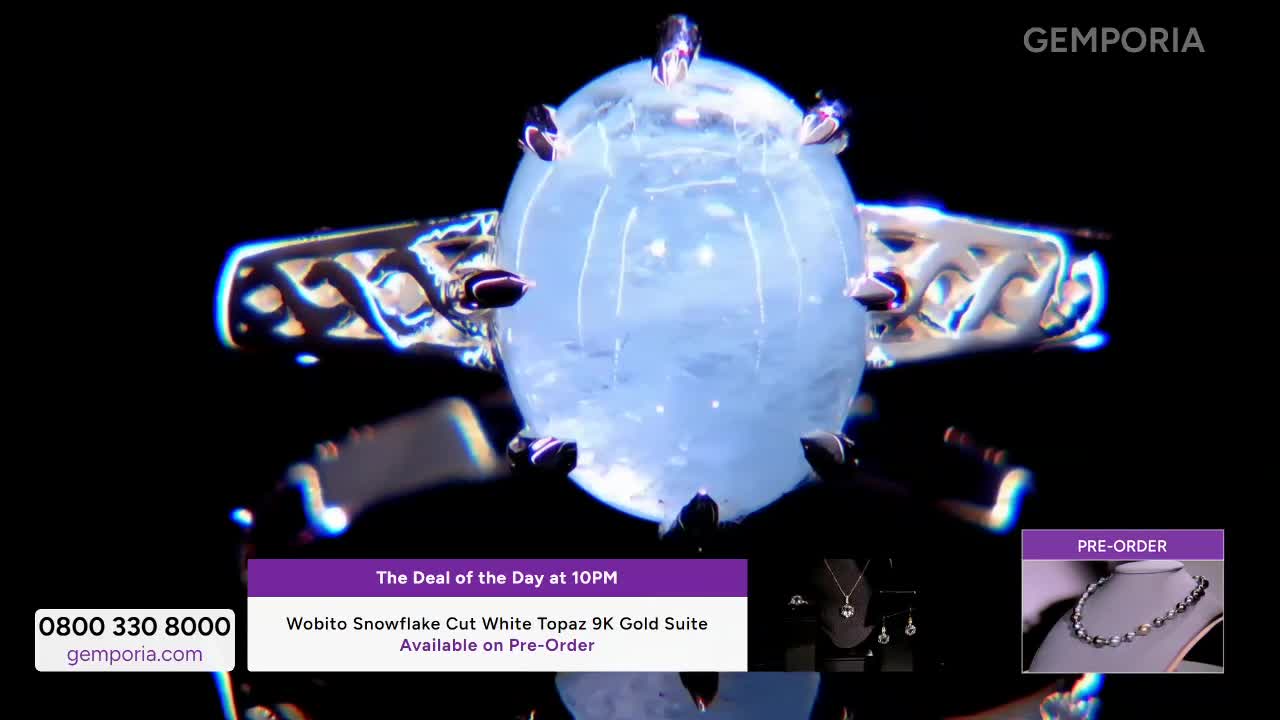 A large, pale blue gemstone on a silver ring slowly turns, catching the light. Below, a banner announces "The Deal of the Day at 10PM" and details a Wobito Snowflake Cut White Topaz 9K Gold Suite available for pre-order.