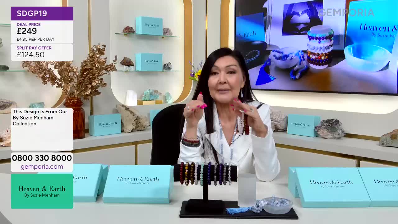 A woman on Gems TV holds up a strand of dark red beads, her other hand gesturing towards a display of bracelets. On the screen behind her, the "Heaven & Earth" logo is prominently featured.