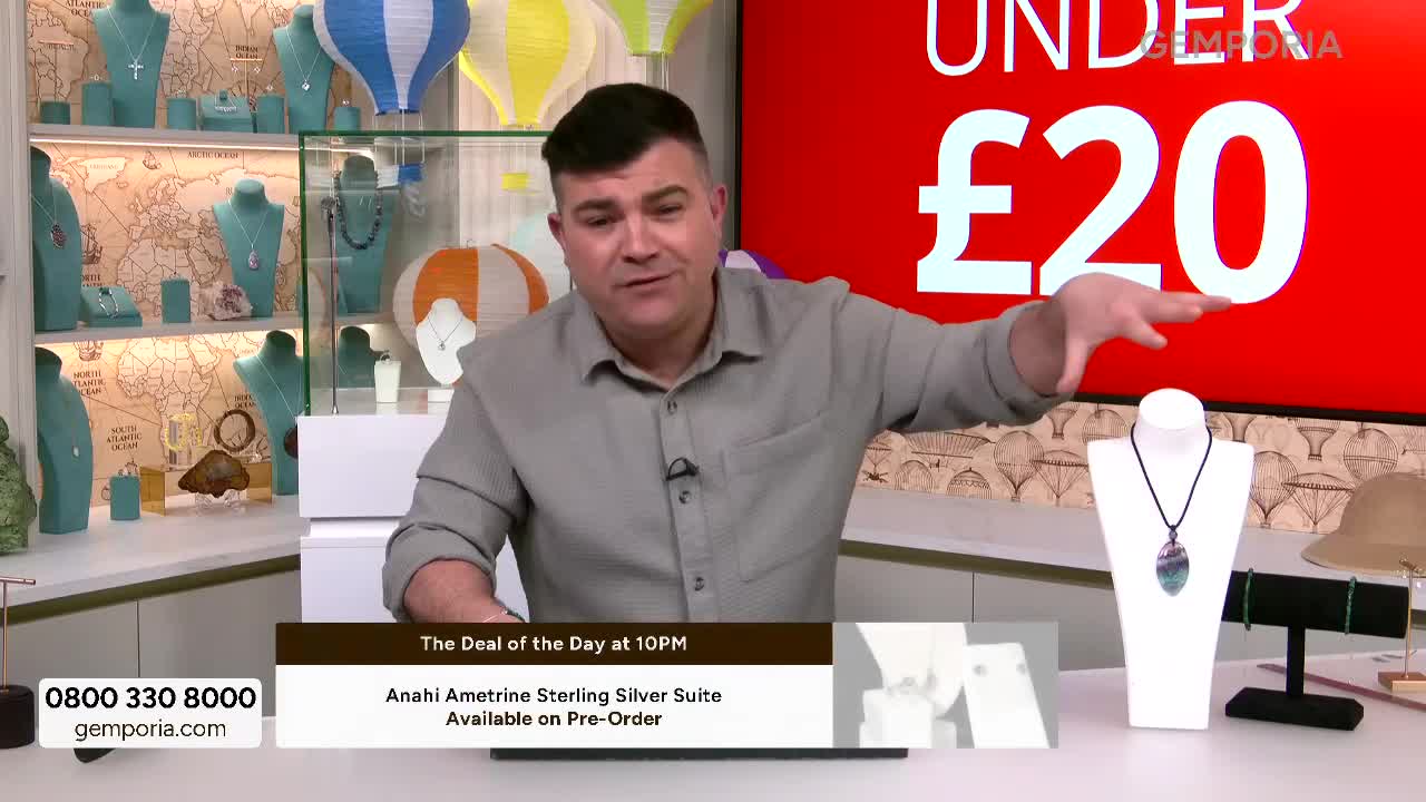 A man gestures towards a display of necklaces on Gems TV. The screen behind him prominently features a red background with "UNDER £20" in large white lettering.