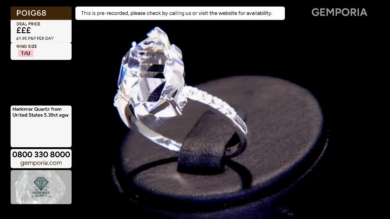 A large, faceted Herkimer Quartz sits on a black stand, its many facets catching the light. The ring band sparkles with smaller stones, a detail that catches my eye as it rotates slowly.