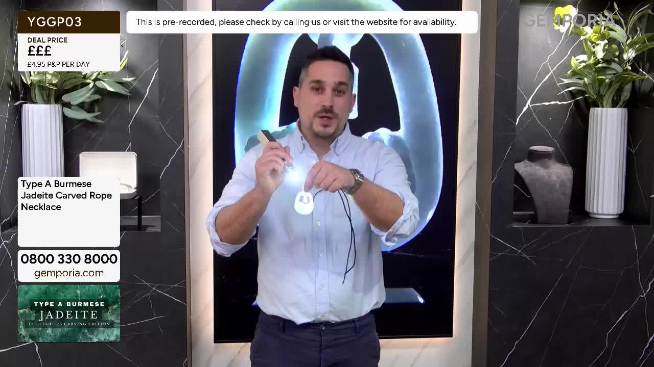 The presenter holds up a white pendant, shining a light on it. He's demonstrating a necklace on Gems TV. The presenter holds up a white pendant, shining a light on it. He's demonstrating a necklace on Gems TV.