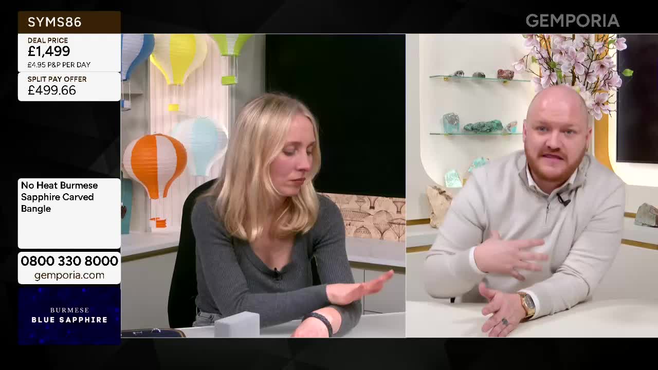 A woman in a grey top gestures with her left hand, showing a dark bangle on her wrist. Beside her, a man in a light grey jumper speaks animatedly, his hands moving as he talks. A woman in a grey top gestures with her left hand, showing a dark bangle on her wrist. Beside her, a man in a light grey jumper speaks animatedly, his hands moving as he talks.