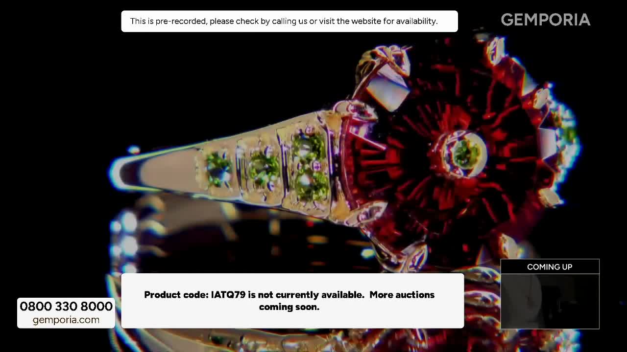 A large, ornate ring with green stones and a deep red centrepiece slowly rotates, catching the light. A message flashes across the screen: "Product code: IATQ79 is not currently available. More auctions coming soon."