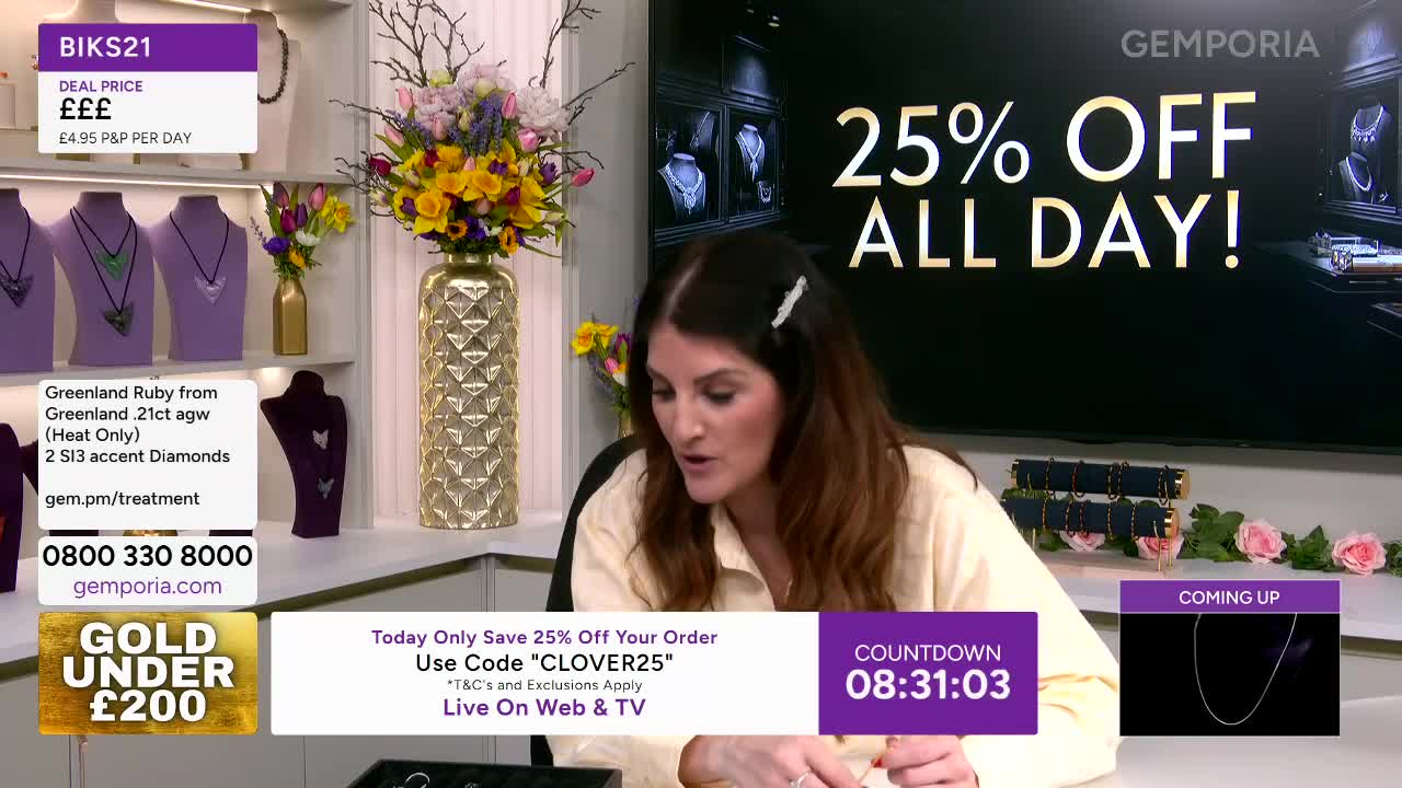 A woman with long brown hair, wearing a light yellow top, gestures with her hands as she speaks. Behind her, a large screen displays "25% OFF ALL DAY!" and a vase overflows with a colourful bouquet of flowers.