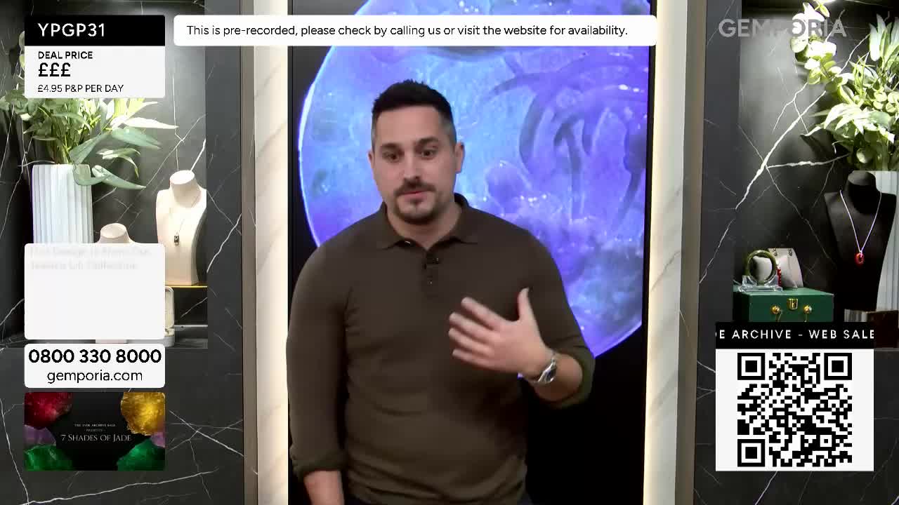 A man in a brown polo shirt gestures with his right hand. Behind him, a large screen displays a swirling blue and purple pattern. A man in a brown polo shirt gestures with his right hand. Behind him, a large screen displays a swirling blue and purple pattern.