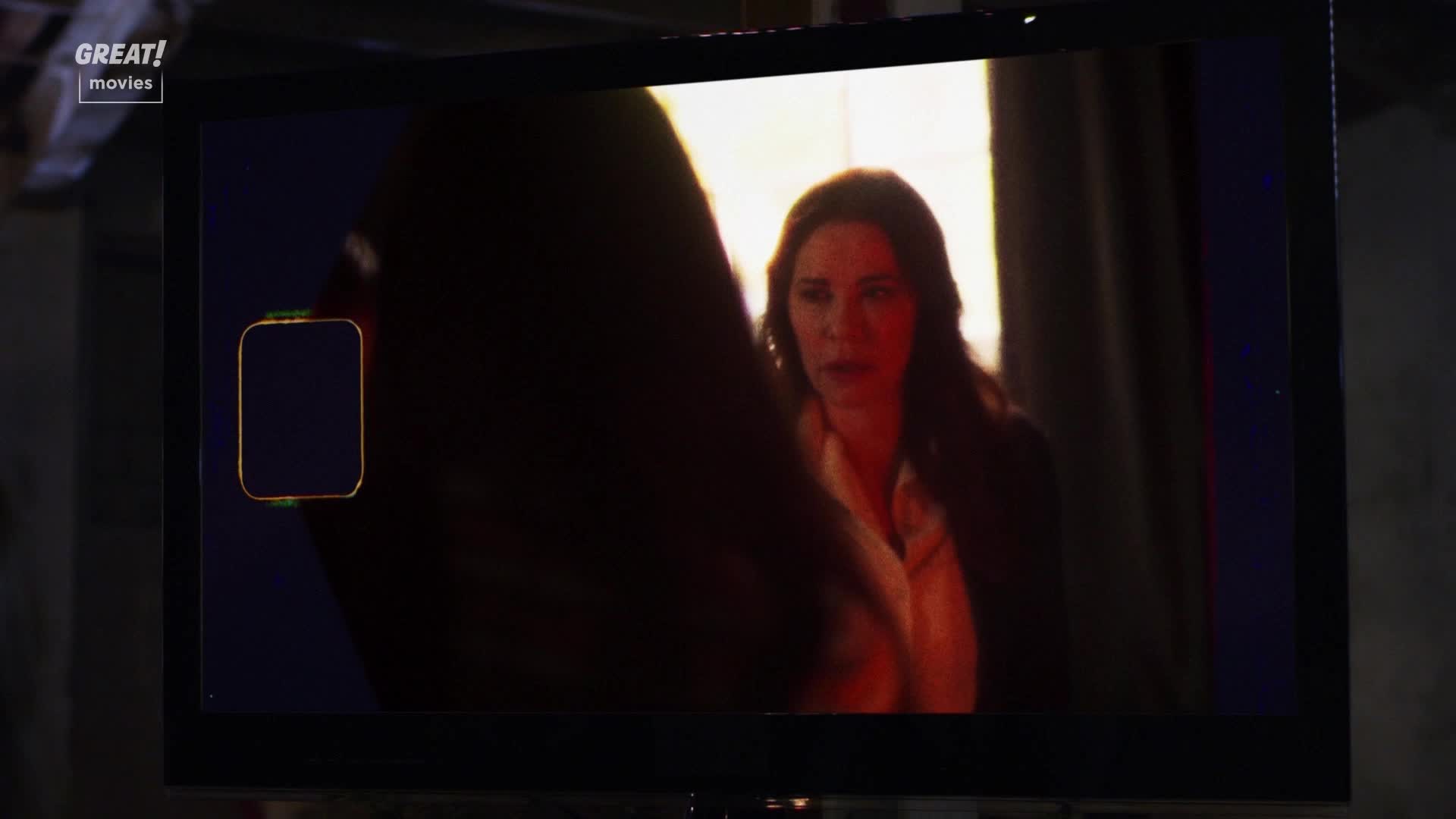 A woman with long dark hair is speaking, her face illuminated by a warm glow.  The scene is framed on a television screen, likely a film from the United Kingdom.
