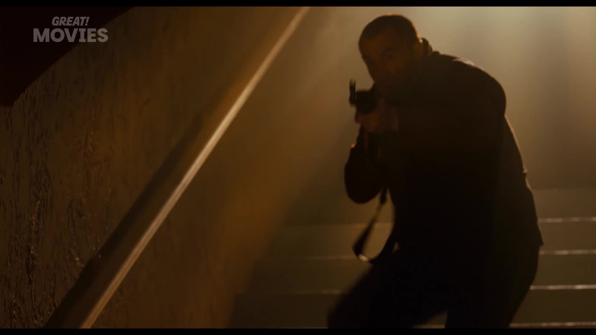 A man in dark clothing descends a staircase, his weapon raised. The scene is dimly lit, the air thick with a hazy fog.
