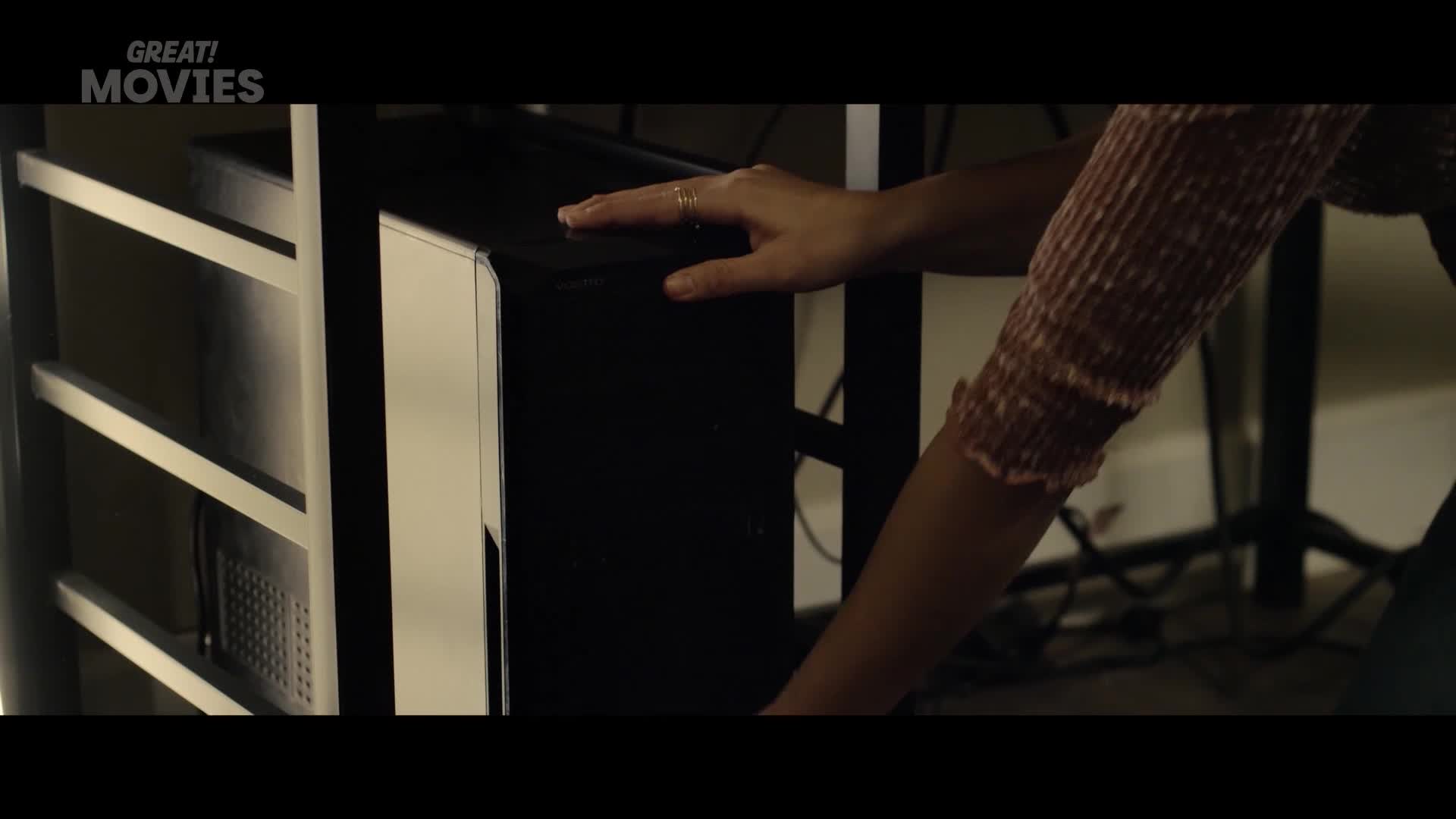 A hand with a ring rests on top of a black computer tower. The sleeve of a pink, textured top is visible.