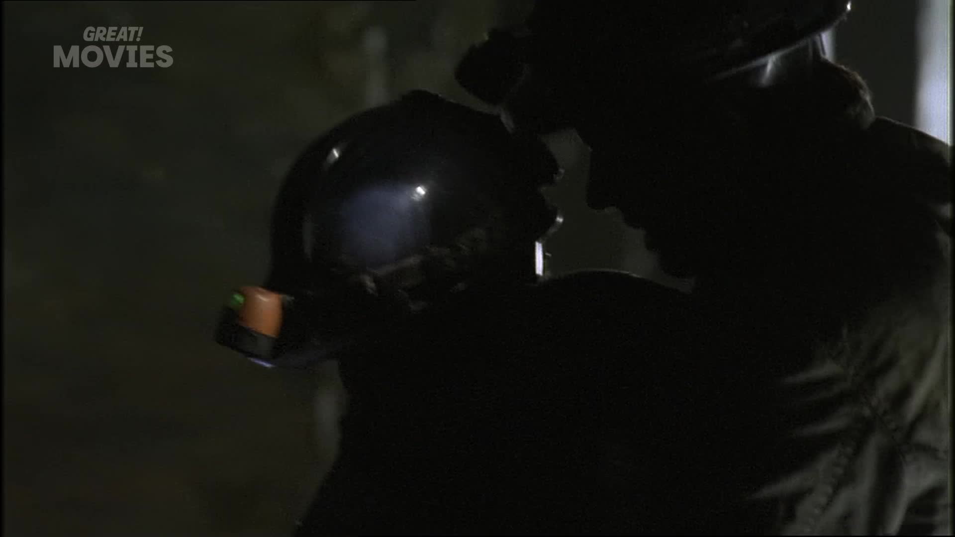 A firefighter, silhouetted against the dark, holds a helmet with a small, bright light attached. Another figure, also in shadow, leans in close.