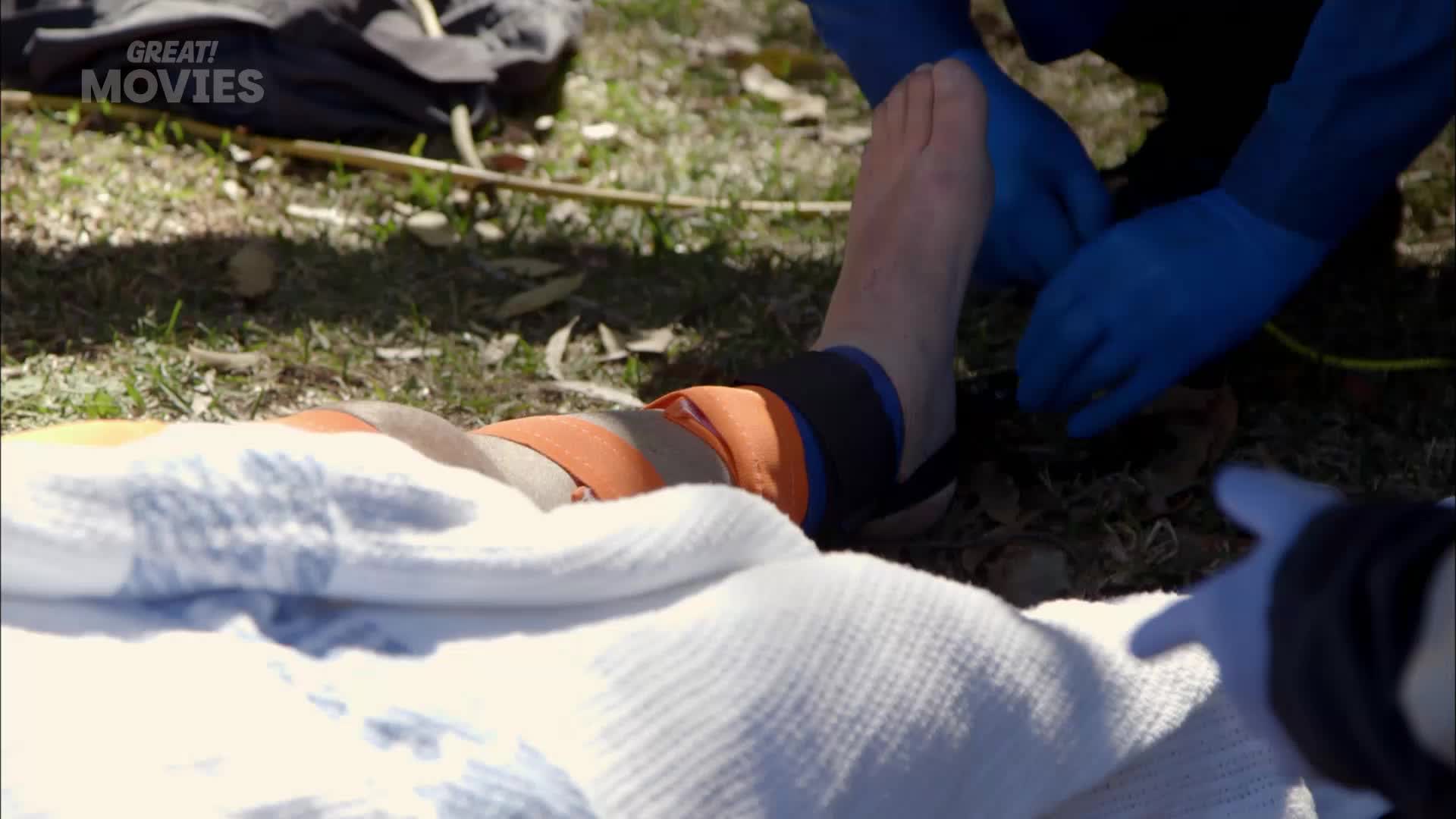 Someone's leg is being bandaged with orange straps.  Gloves are on, and a white blanket covers the rest of them.