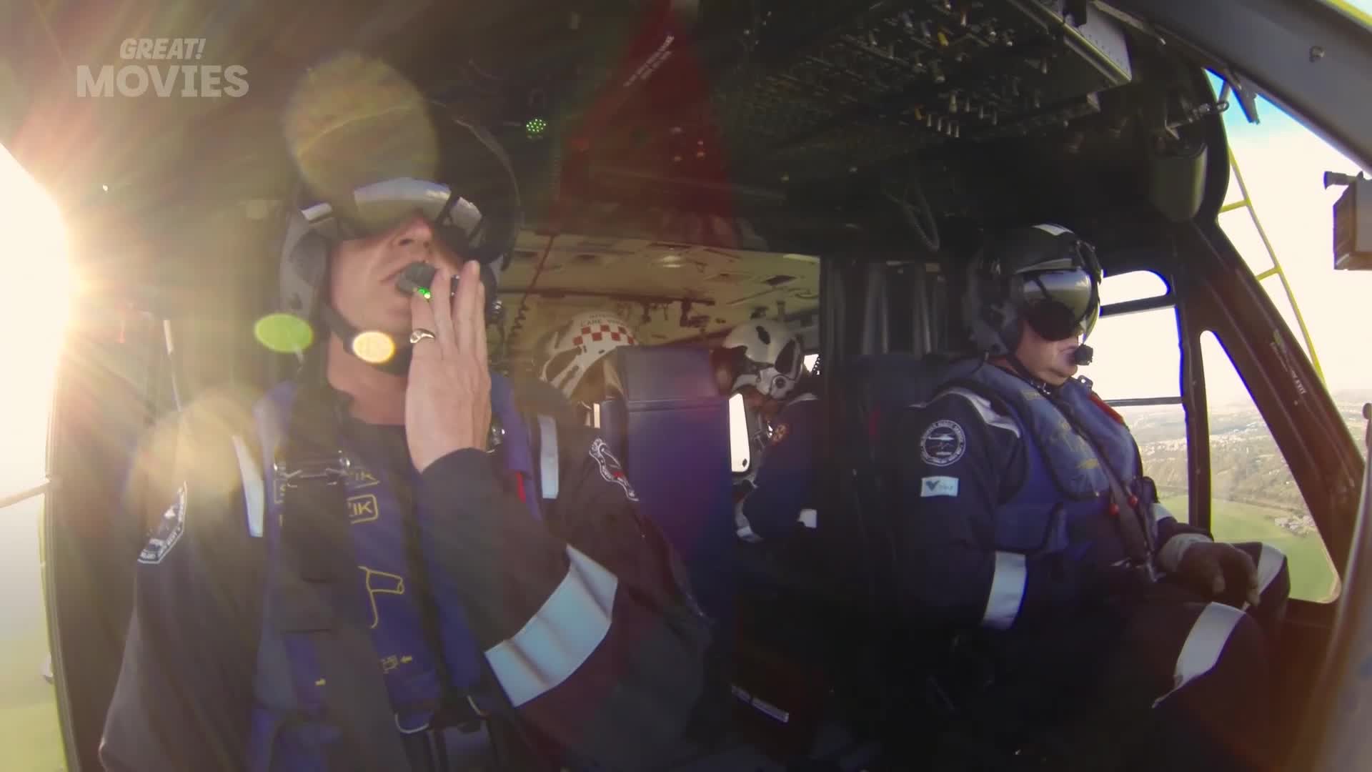 The pilot in the front left is speaking into a microphone, his hand raised to his face. Beside him, the co-pilot is focused on the controls, his gaze fixed ahead.