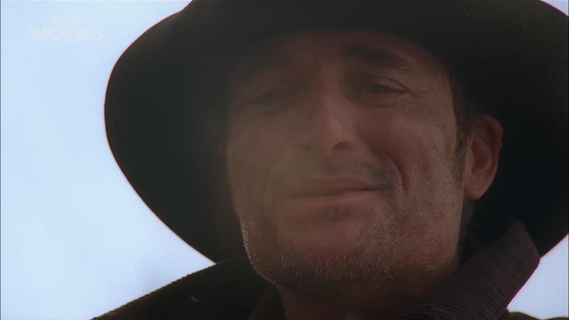 The man's weathered face, framed by a wide-brimmed hat, is turned slightly towards me. A faint smile plays on his lips, his eyes squinting against the bright sky.