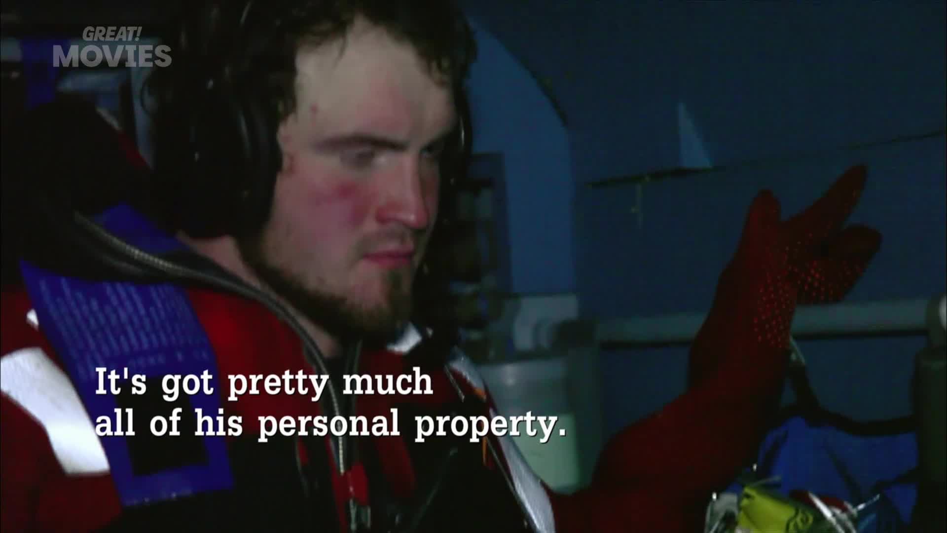 A man in a life vest and headphones looks intently ahead. His gloved hand, dotted with red grips, is raised as if to signal.