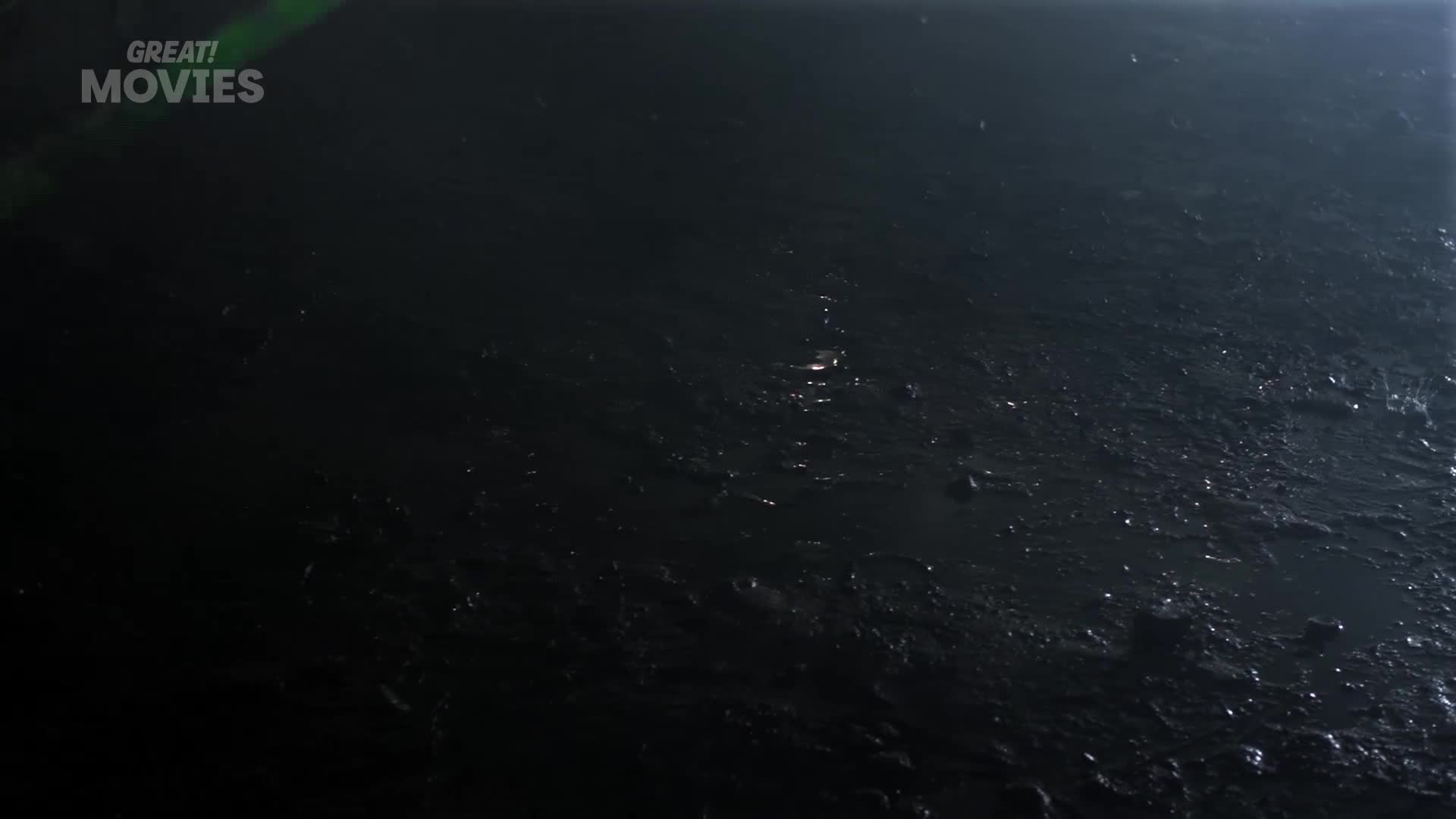 A faint green light slices across the dark, rippling surface of what looks like a canal or river. The water is murky, reflecting small glints of light as it moves.