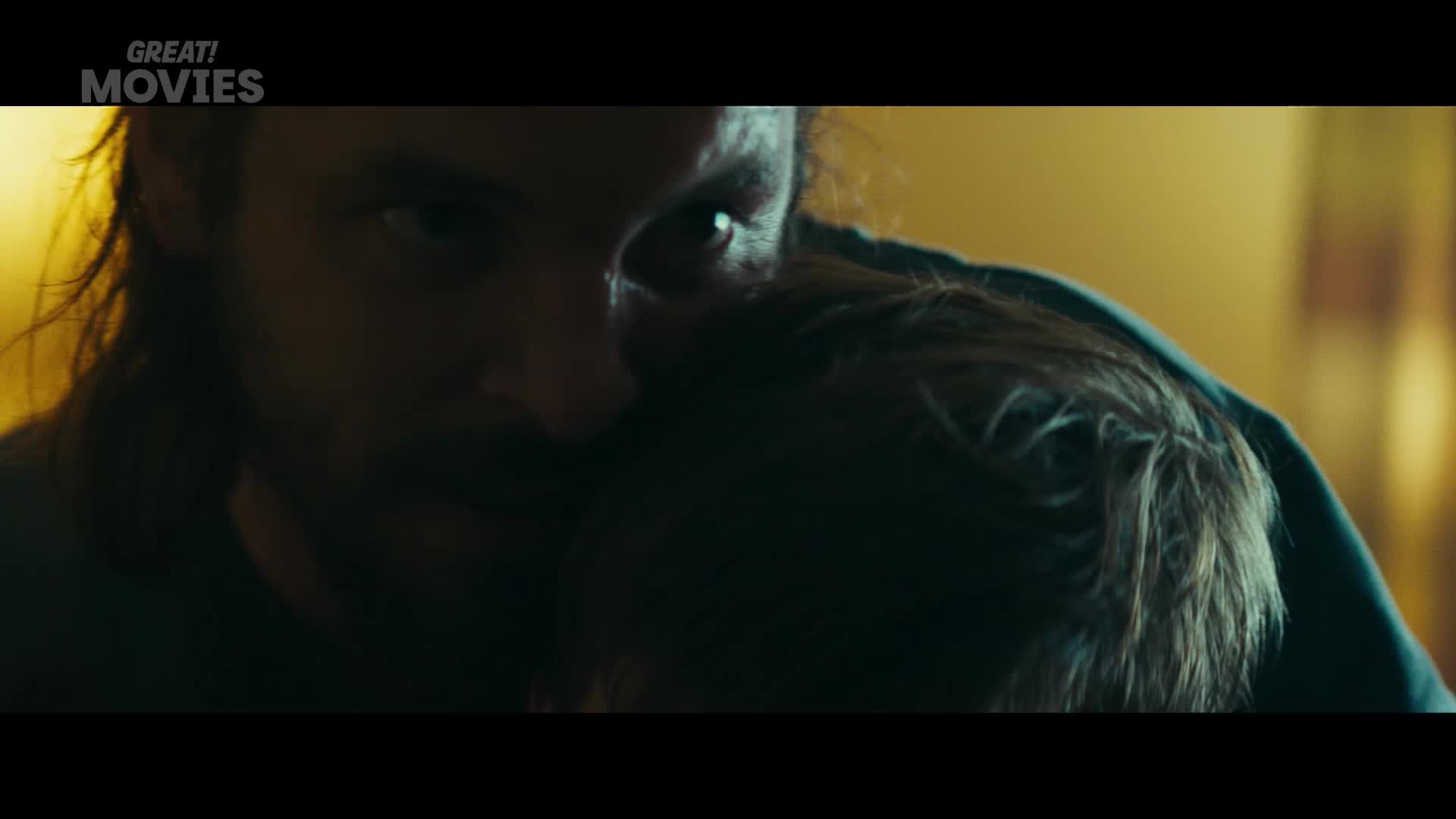 A man with long hair leans in, his eye intense. He holds a child close, their heads together.