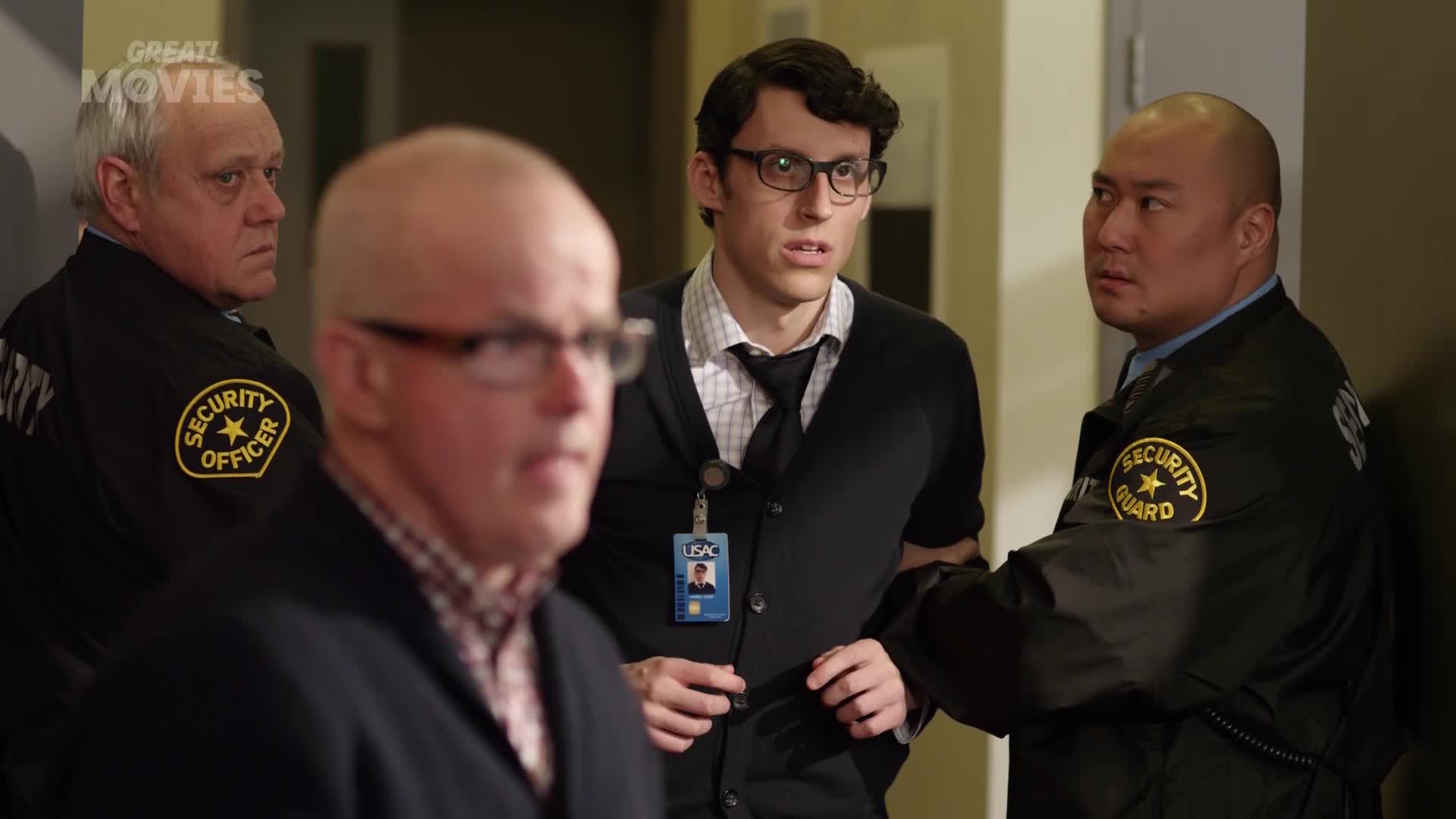 Two security guards are escorting a nervous-looking man in glasses. Another guard stands nearby, watching intently.