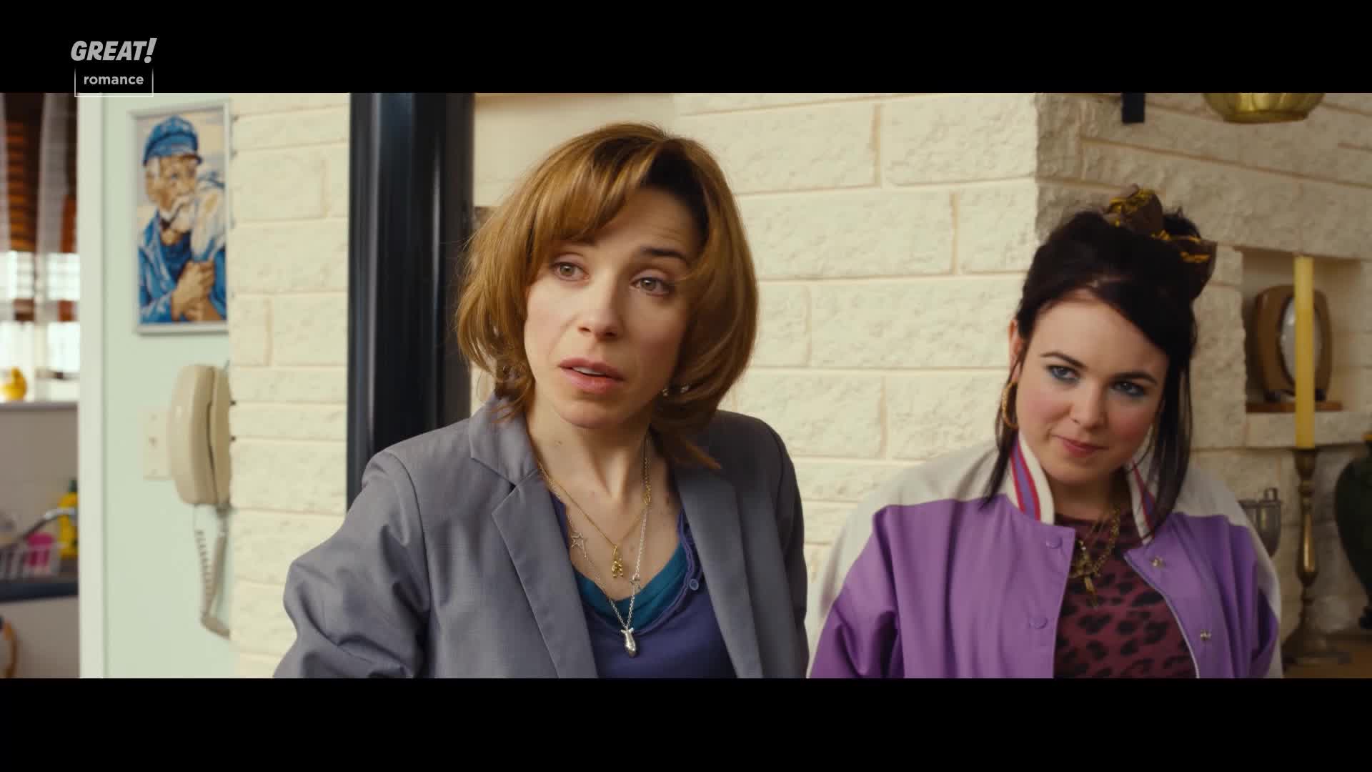 The woman in the grey jacket looks concerned, her gaze fixed on something just out of frame. Beside her, the other woman, in a purple jacket, watches with a knowing expression.
