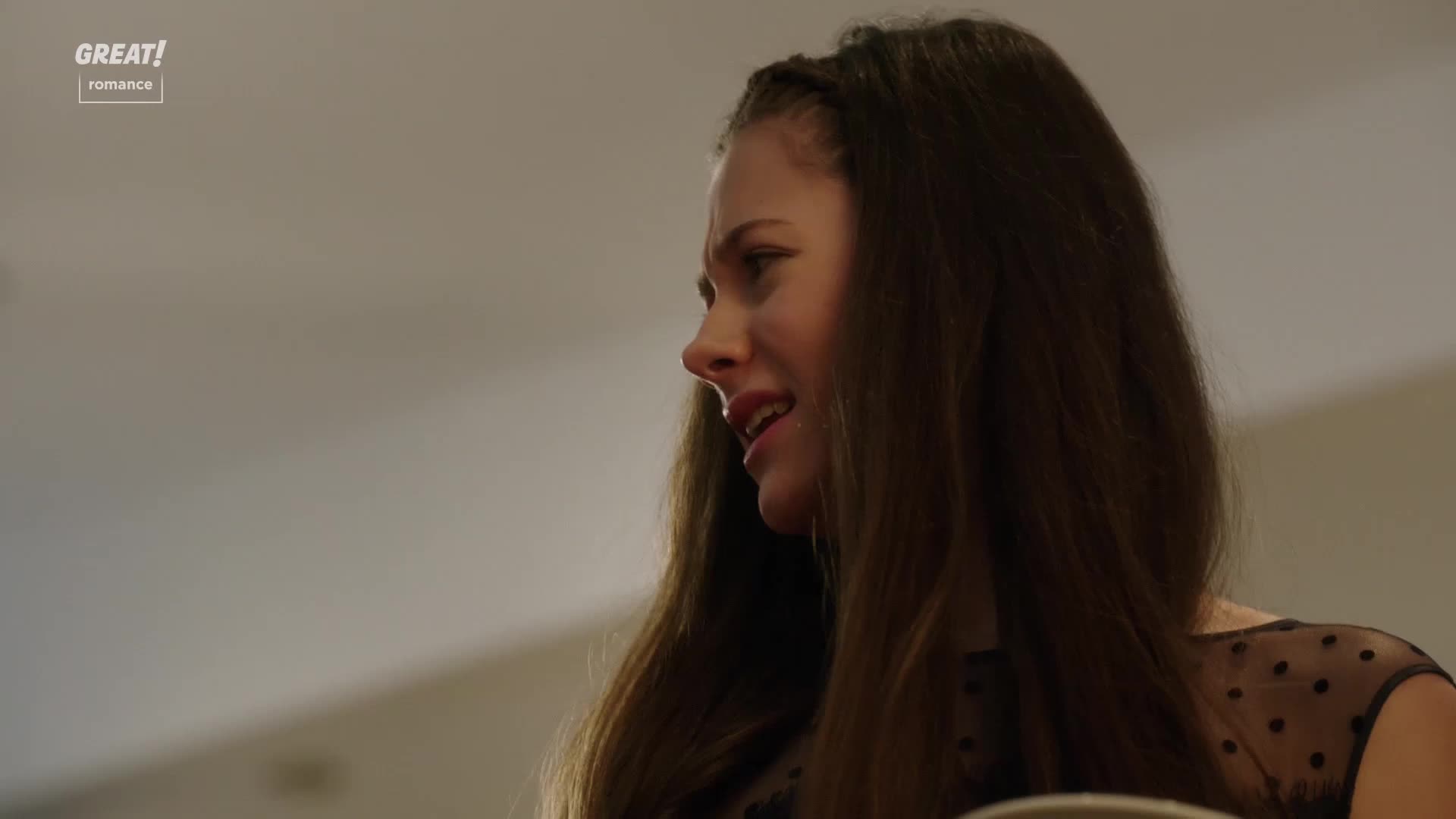 Her face is contorted, tears welling in her eyes as she speaks. The dark hair is parted and styled in a braid, and she's wearing a sheer-sleeved top.
