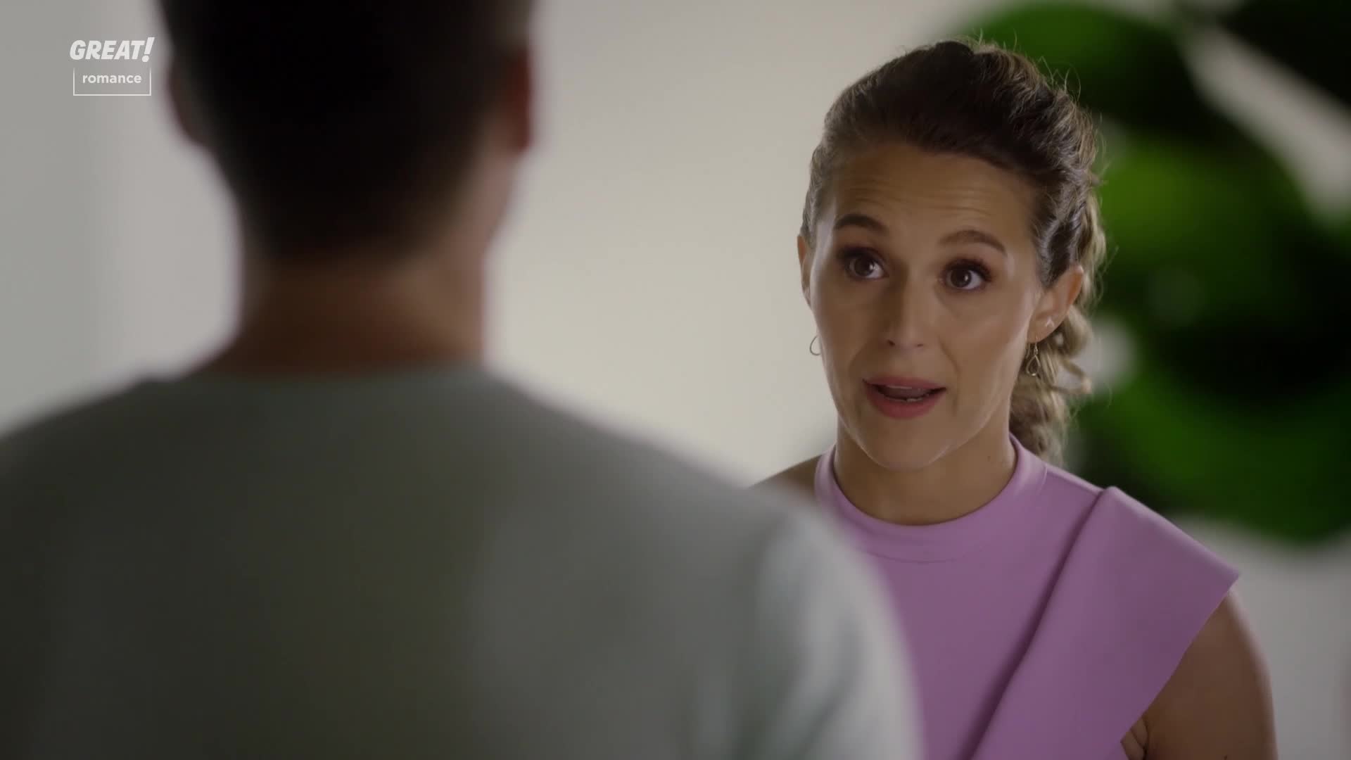 She's speaking, her mouth open, and her eyes are focused on the person in front of her. The woman's wearing a lilac top, and her hair is pulled back.
