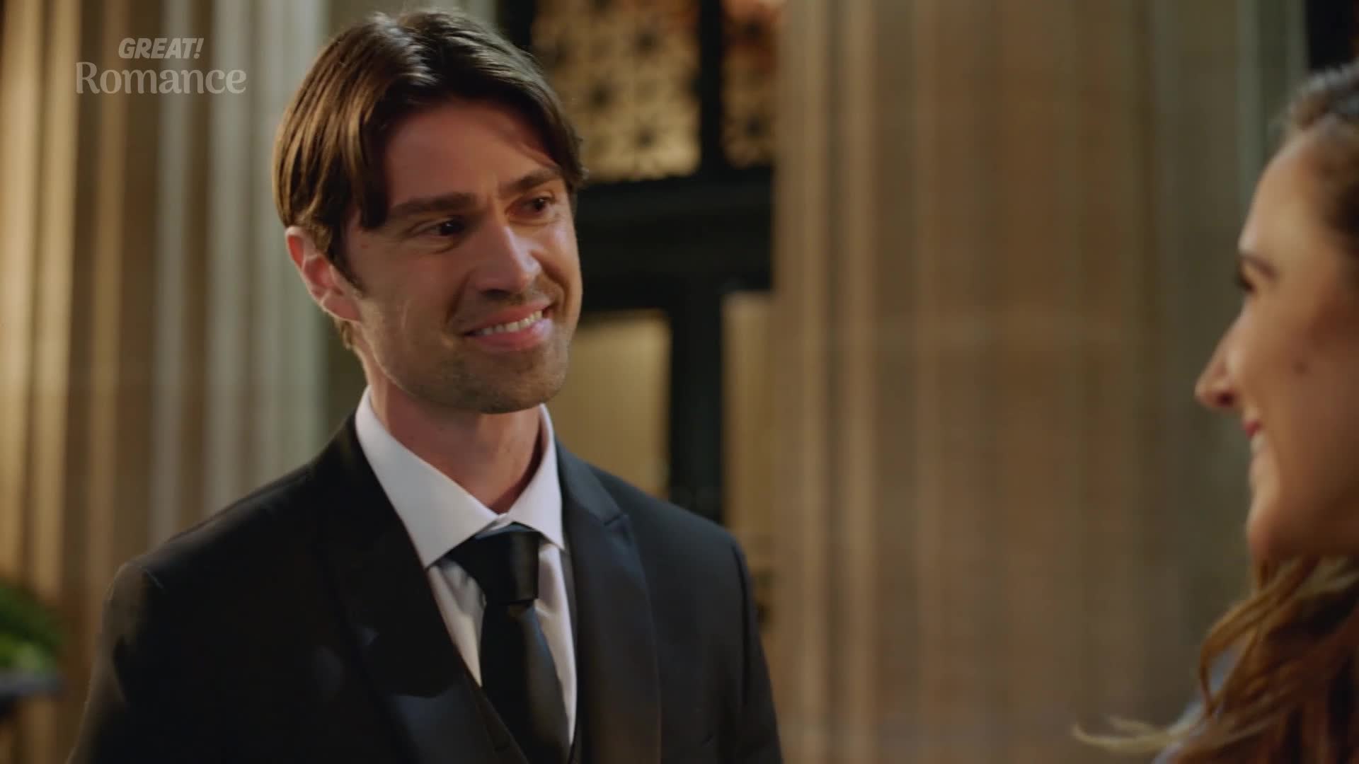 The man in the tuxedo is smiling, his eyes crinkling at the corners. He's looking at someone just out of frame, and the scene has a romantic air.
