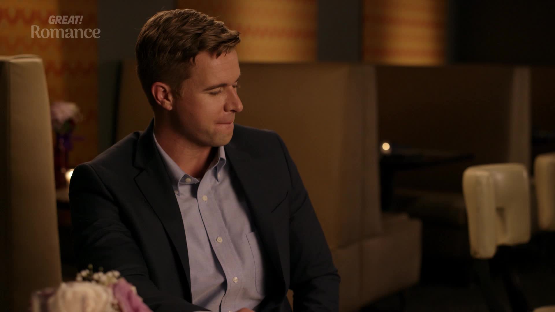 The man in the dark suit looks away, a slight smile playing on his lips. He's seated in a booth, the warm lighting of the restaurant casting a soft glow. The man in the dark suit looks away, a slight smile playing on his lips. He's seated in a booth, the warm lighting of the restaurant casting a soft glow.