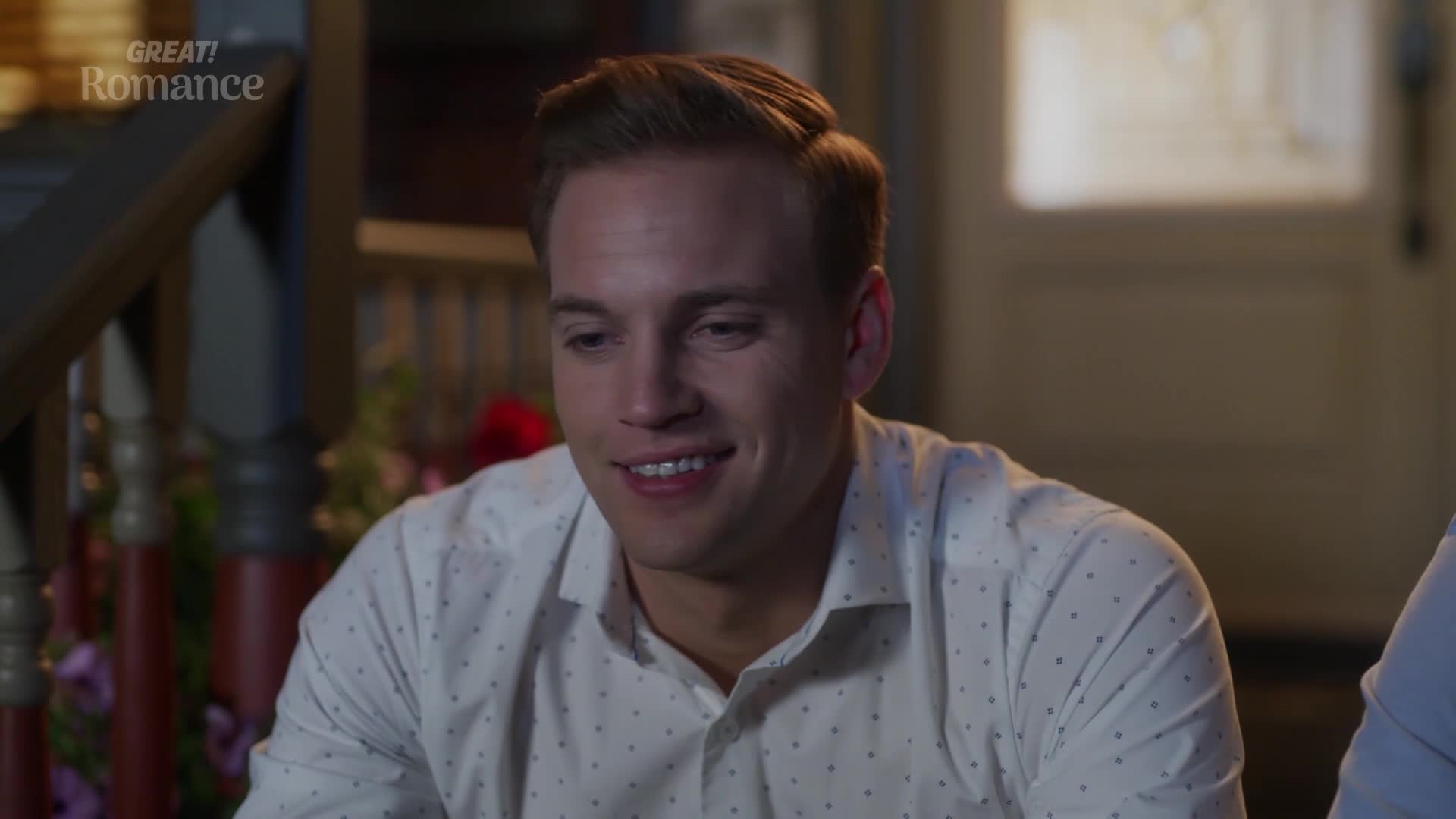 A man with neatly styled hair smiles, his eyes crinkling at the corners. He's wearing a crisp white shirt dotted with tiny dark patterns.