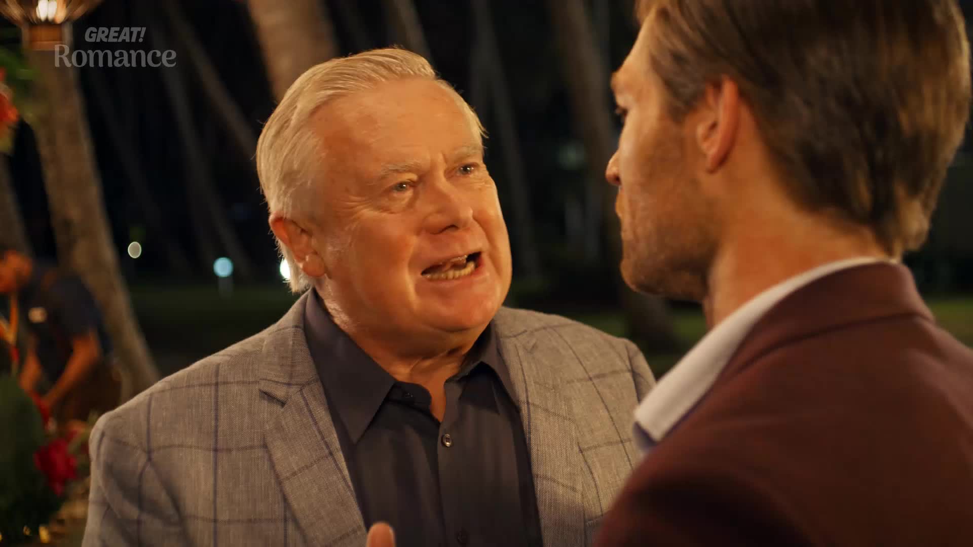 An older gentleman, his face animated, speaks intensely to a younger man. The younger man, seen from the side, listens intently, his expression unreadable.