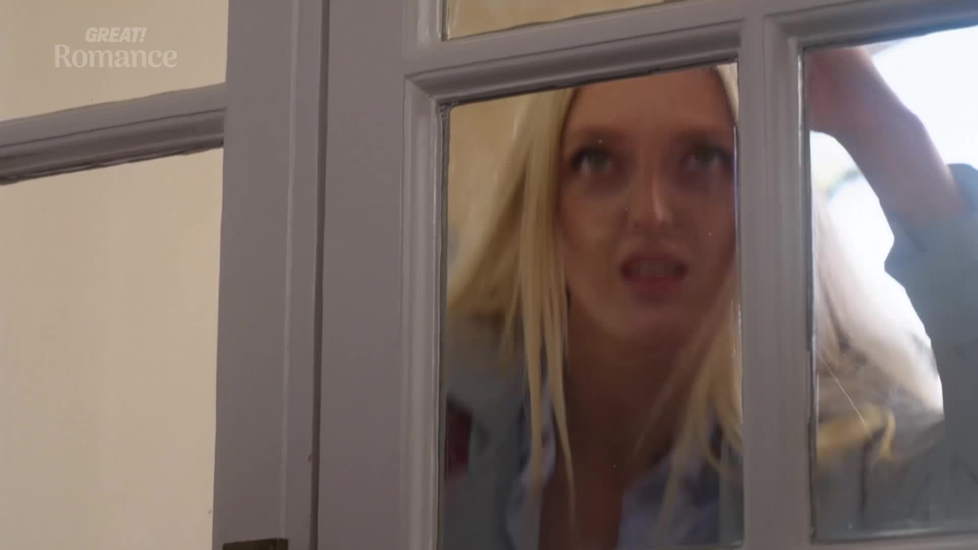 A young woman with blonde hair peers through a glass-paned door, her expression one of concern. The "GREAT! Romance" logo is visible in the upper left corner.