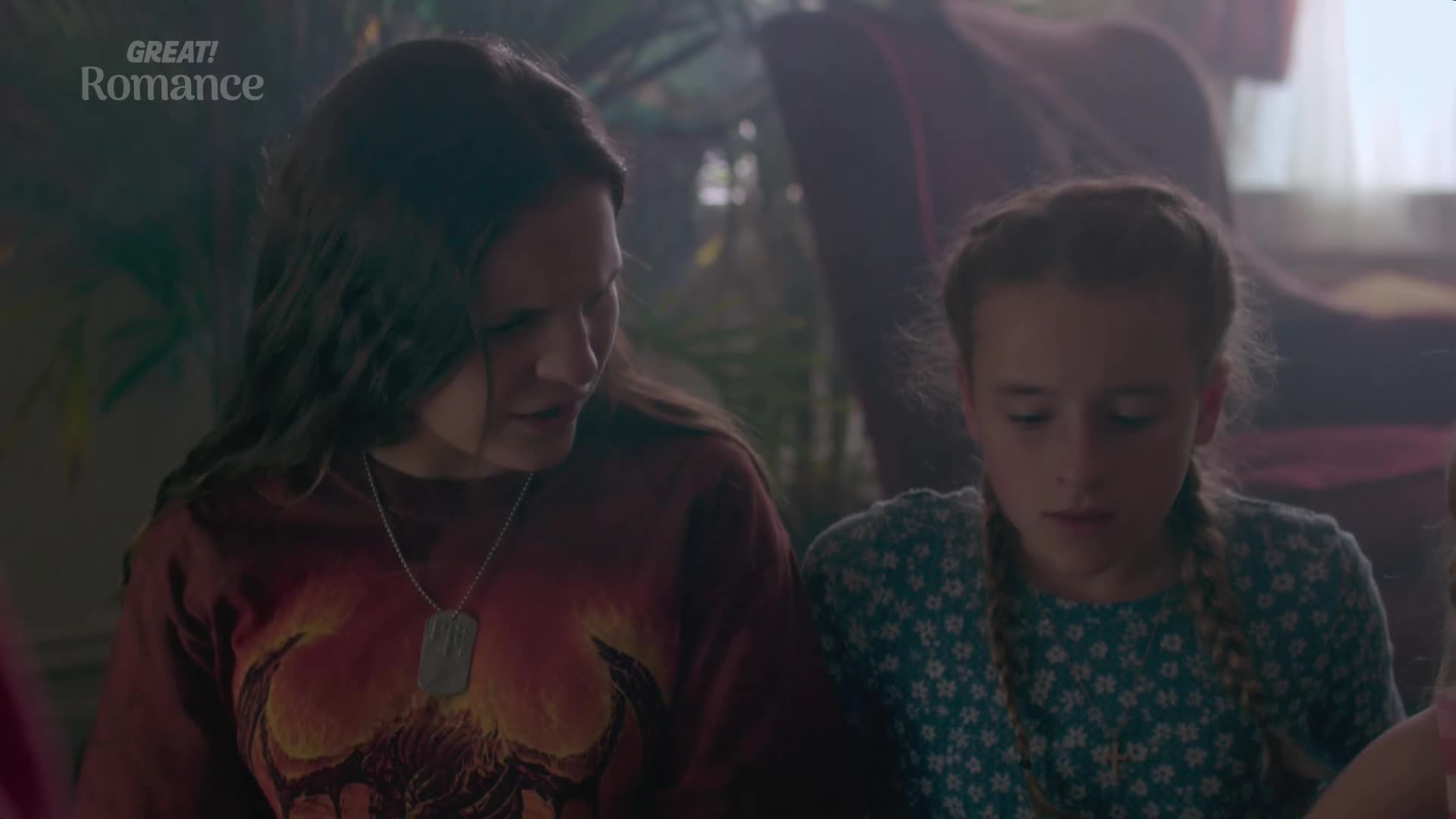 A young woman with dark hair leans in, her expression concerned as she speaks to a girl with braided hair. The girl, wearing a blue floral dress, looks down with a troubled gaze.
