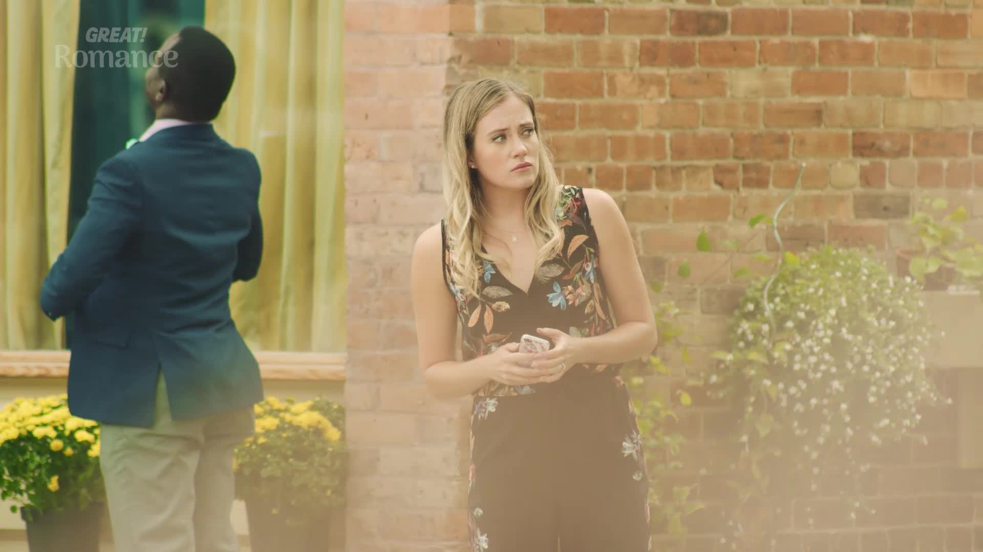 A man in a dark suit stands with his back to me, facing a window. A woman in a floral jumpsuit looks away, her expression thoughtful.