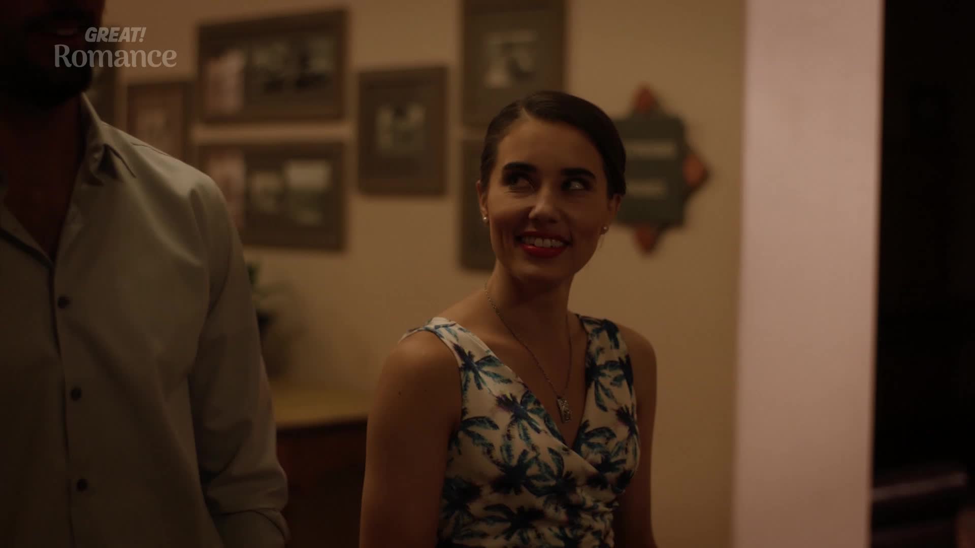 A man in a pale blue shirt stands to the left, his shoulder visible. Beside him, a woman in a floral dress smiles, her gaze directed upwards.