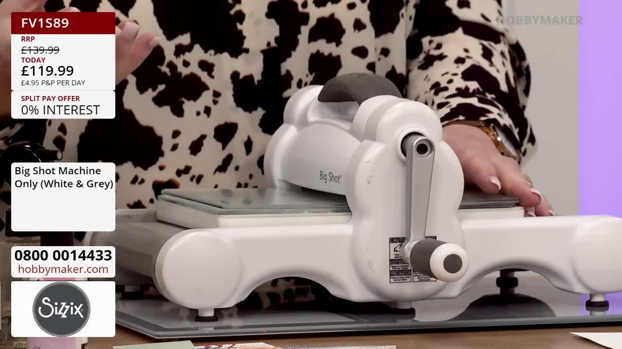 A woman in a patterned top is demonstrating a white and grey Big Shot machine, turning the handle. The Hobby Maker logo is visible in the corner, along with the price.
